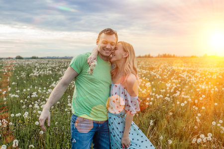 Romantic sunset photo of a happy couple hugging in a field with dandelionsの写真素材