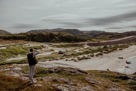 Male traveler stands on top of a mountain and looks into the distance at the sea and the mountains of the tundra, Teriberkaの写真素材
