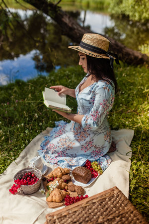 Girl in straw hat reads book lying on blanket in nature in summer at picnicの写真素材