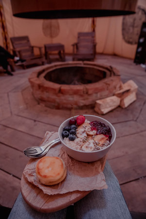 Bowl breakfast with porridge, fruits, berries and nuts and cheesecake on the background of a campfireの写真素材