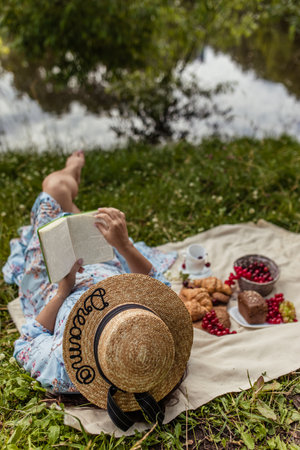 Girl in straw hat reads book lying on blanket in nature in summer at picnicの写真素材