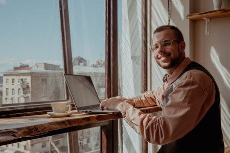 Man with glasses by the window working at a computer on a sunny day. high quality photoの写真素材