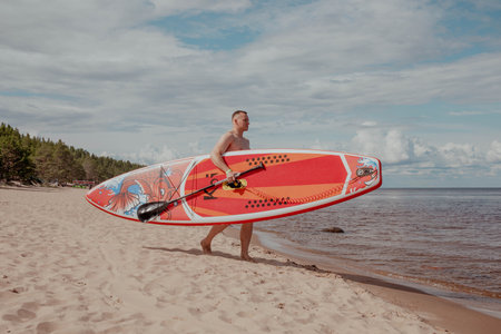 Man walks along the beach with sup board.の写真素材