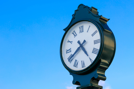 Retro green clock on pillar with roman numerals and blue sky backgroundの写真素材
