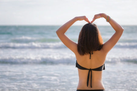 Back view of Travel asia woman with black bikini making heart sign on sea beach in summer, Koh Samet, Thailandの写真素材