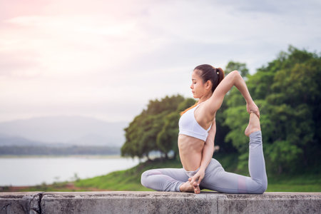Asia woman with sport bra doing yoga fitness exercise for relax and healthy at lake in morning, Nature background, Concept outdoor sport and healthの写真素材