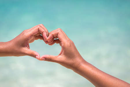 female hands in heart shape on sea beach at day time background, Summer seasonの写真素材