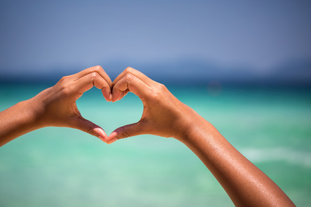 female hands in heart shape on sea beach at day time background, Summer seasonの写真素材
