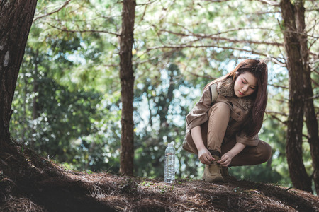 Adventure young asia woman resting with fresh water bottle and check the shoestring in green forest at day, summer travel conceptの写真素材