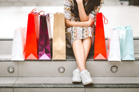 Lifestyle shopping concept, Young happy smiling woman with paper bag sit on staircase in shopping street at evening, vintage styleの写真素材