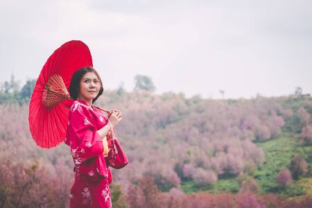 Asia woman with kimono and red Japanese umbrella against sakura flower backgroundの写真素材
