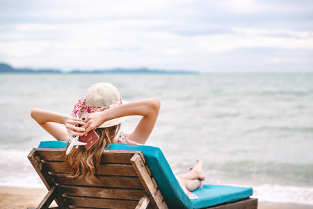 Summer travel vacation concept, Happy asian traveler woman holding passport and plane model relax on beach chair in tropical beach at Thailandの写真素材