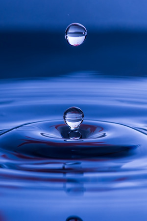 Water droplets about to fall into rippling waterの写真素材