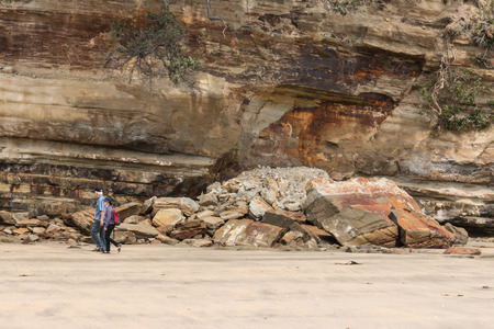 people walking past rockfall on beachのeditorial素材