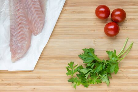 fish fillets with cherry tomatoes and fresh parsley leaves on wooden boardの写真素材