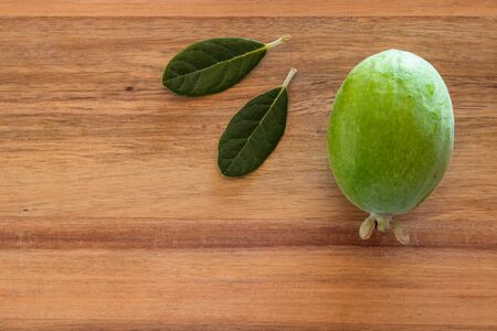 ripe feijoa fruit and leaves on wooden chopping board with copy space on leftの写真素材