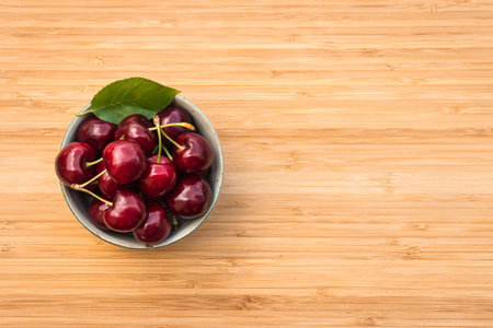 closeup of ripe dark red cherries in porcelain bowl on wooden chopping board with copy space on rightの写真素材