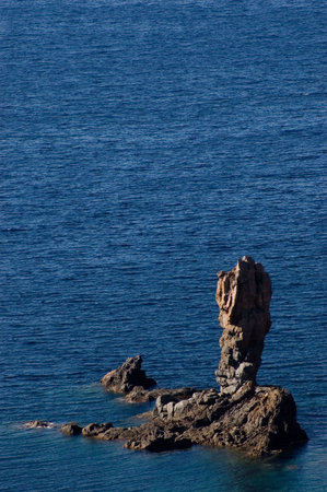 Little steep stone island near Corsica seashoreの写真素材