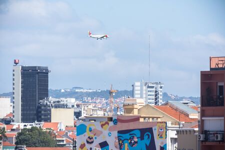 commercial airplane flies over roofs of lisbon lovely summer day portugalの写真素材