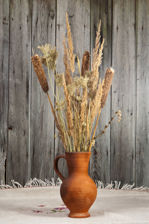 Clay jug with a bouquet of a dry reeds on old wooden backgroundの写真素材