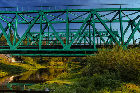 Green metal railway bridge through the small river