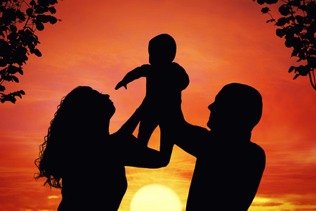 Parents with their little child at sunset, raising baby up in the air. Silhouette of a happy family of three people, mother, father and babyの写真素材