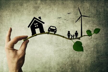 Human hand holding a tree branch. Environmental green energy concept. Silhouette of happy family, house, car and windmillの写真素材