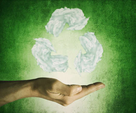 Opened hand holding recycling symbol from clouds on a green background. Friendly environment and sustainable development conceptの写真素材