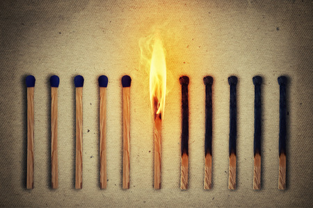 Burning match standing middle a row of whole, new matches at left and extinguished at right. Leadership conceptの写真素材
