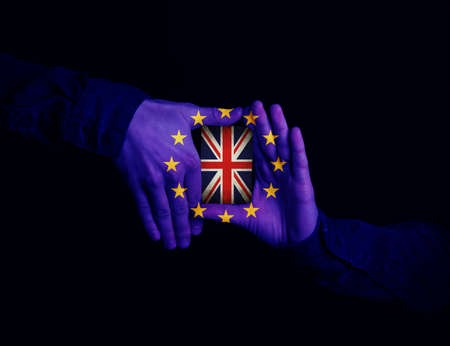 Close up of hands patterned with the flag of the European Community holding a card with the flag of the United Kingdom. Magician showing his trick with cards on black backgroundの写真素材