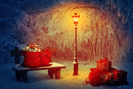 Lot of presents with Santa sacks in the park. Wooden bench and a shining lamp in the snowy night. Peaceful Christmas scene and winter holiday gifts. New Year celebration background.の写真素材