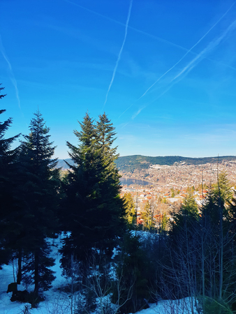 Evergreen coniferous trees on the top of mountain hills in a spring day with picturesque view to the village. Snow melting and a sunny blue sky.の写真素材