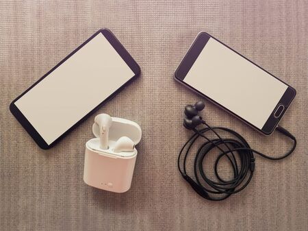 Comparison between two phones, one has 3.5mm jack wired headphones vs wireless earphones for music listening. Pros and cons, opposite contrary. Technology development tendencies, entertainment conceptの写真素材