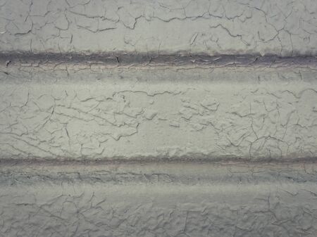 Grey paint peeling off a metallic surface background. Old grungy, weathered painted wall texture. Cracked, dirty, silver plaster falling off the construction structure.の写真素材