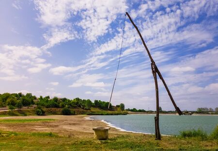 Idyllic countryside scene with an old water well sweep (shadoof) near the Delia lake (Moldova). Also called a counterpoise lift or well pole, is an ancient irrigation tool and used for watering crops.の写真素材