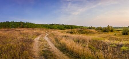 Idyllic autumn rural panorama with and a country track across a meadow with dry grass and hay. Beautiful evening scene, peaceful sunset light over the steppe vegetation.の写真素材
