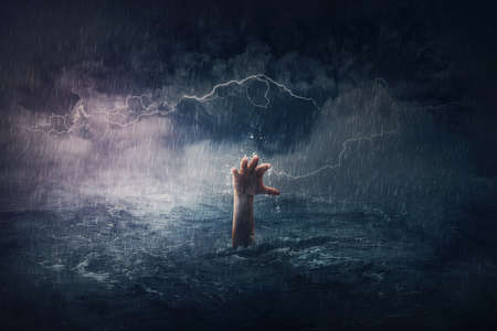 Arm drowning in the sea. Surreal and dramatic scene of person hand sinking in the ocean under a hurricane stormy weather. People need help in risk situations. Despair, depression and failure metaphorの写真素材