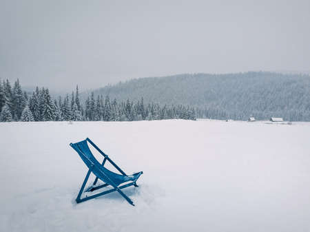 Sunbed type chair on the top of a mountain in a snowy winter day. Fir forest covered with snow on the horizon. Bukovel ski resort, Ukrainian Carpathians. Blizzard scene, seasonal travel backgroundの写真素材