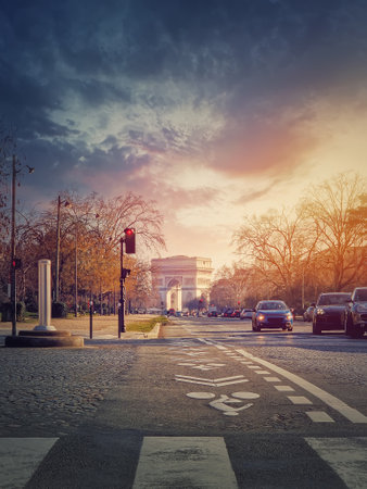 Triumphal Arch (Arc de triomphe) in Paris, France. The famous historic landmark in sunset light seen from the city street with busy trafficの写真素材