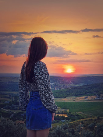 Rear view of a girl watching the sunset from the top over the valley. Natural summer evening sceneの写真素材