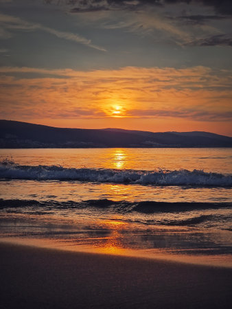 Early morning at the beach with vibrant sunrise at horizon and foamy waves hitting the sand. Dawn at the sea, peaceful viewの写真素材