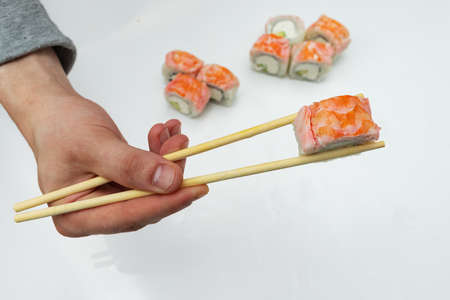 hand holding sushi sticks, against the background of a large portion of rice dishes of Asian cuisine, food with traditional toolsの写真素材