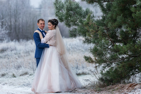 newlyweds walk along the winter street embracing together, joyful emotions of lovers during a wedding walk in the snowfall around the cityの写真素材