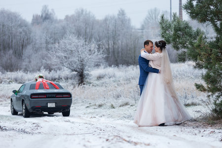 newlyweds on a wedding walk in winter stand together and pose for a photographer near a snow-covered tree in a beautiful forest, family photo shoot and loveの写真素材