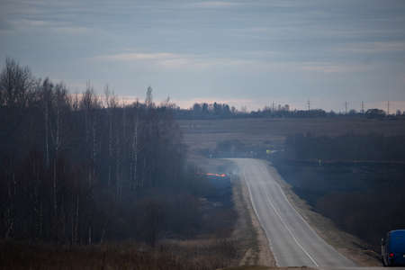 a strong forest fire breaks out in windy weather due to human fault, flames destroy dry grass on the edge of the forest and fields in early spring, call the fire brigade to extinguish the fireの写真素材