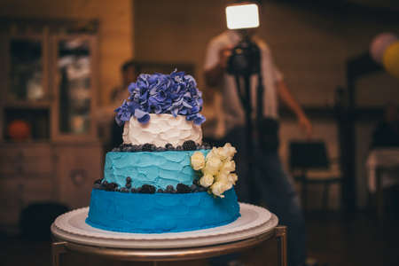 Wedding cake decorated with blue flowers on a stand in a restaurantの写真素材