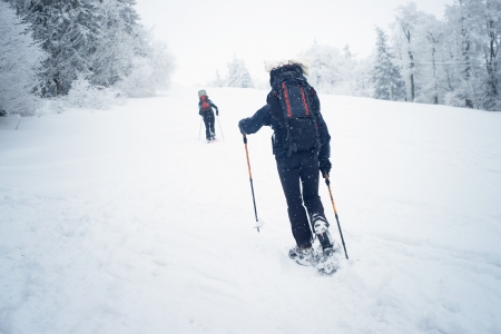 Two tourists are walking uphill in winter time on the snow with snowshoesの写真素材