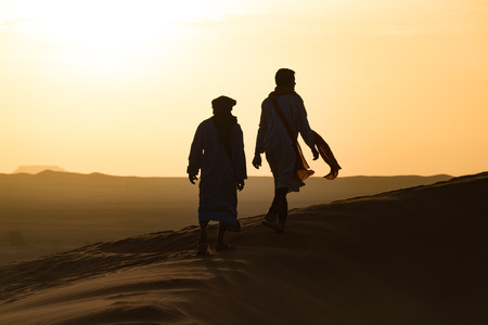 Silhouette of Berber and camel at bloody red sunset, Merzouga in Morocco, Sahara Desert, North Africa.の写真素材