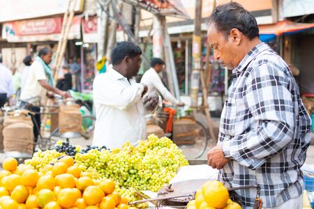 India, Varanasi, Mar 10 2019 - Unidentified vendor man sells and weighs grapes on traditional street food market.のeditorial素材