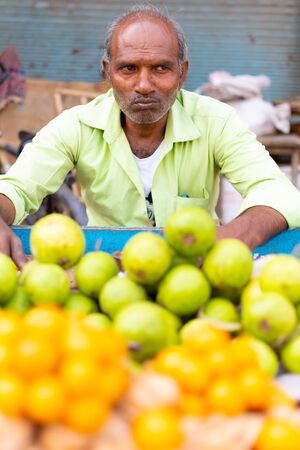 Varanasi, India, Mar 10 2016 - Indian vendor sits in front of a pile of fresh green sugar apples and orangesのeditorial素材